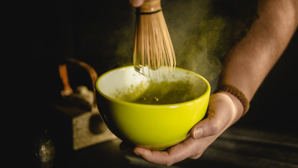 Hot drinks from around the world represented by a close-up of someone making matcha using a matcha whisk.