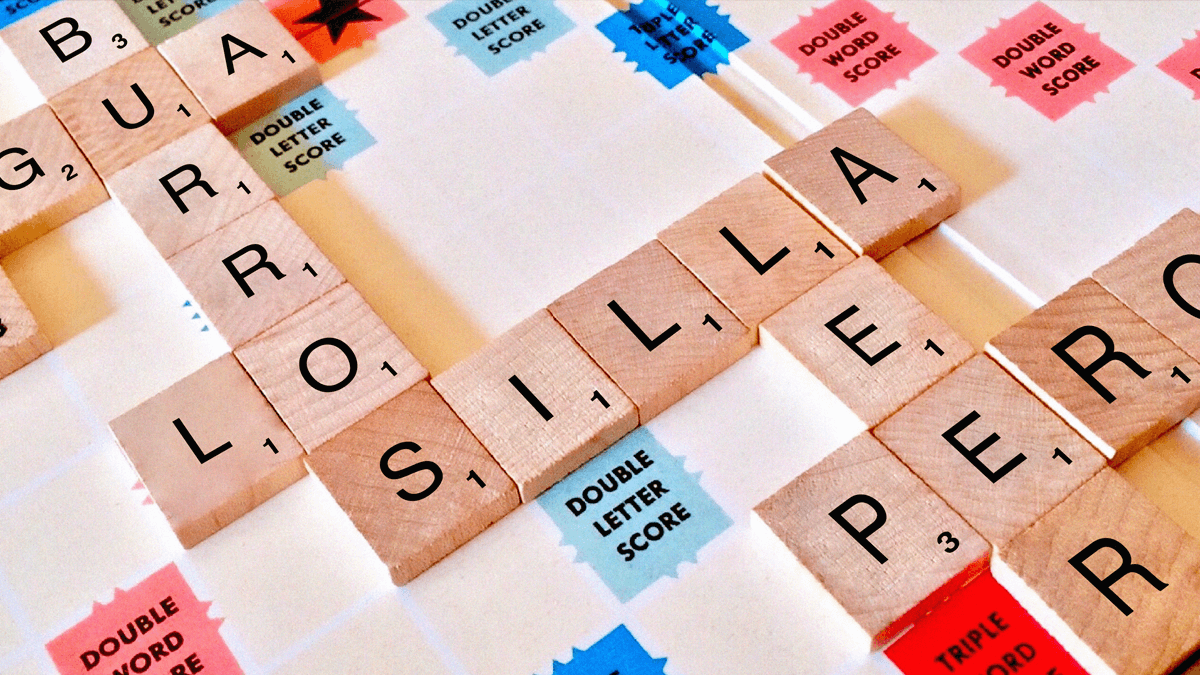 Language games represented by a scrabble board covered in tiles with Spanish words, including burros, silla and pero.