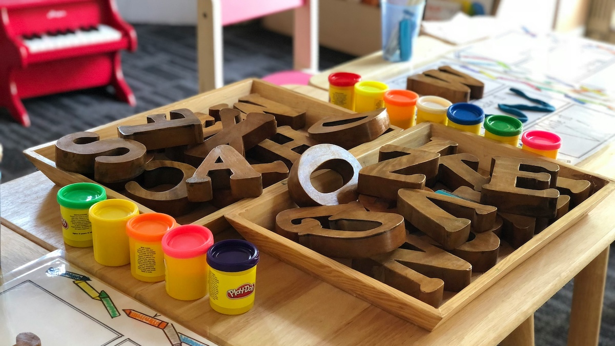 English vowel sounds represented by wooden letters in a children's room surrounded by Play-Doh and other art supplies.