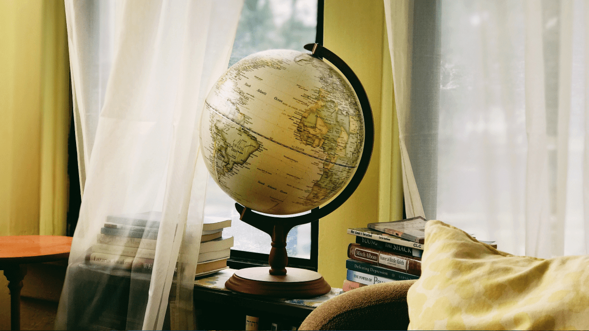 Continent etymology represented by a pale globe showing the continents of the world, placed in front of a window draped with see-through white curtains.