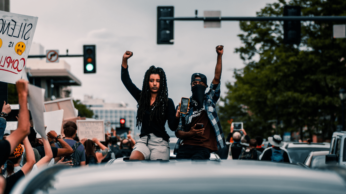2021 words of the year represented by two people holding their fists in the air in solidarity with the surrounding protest
