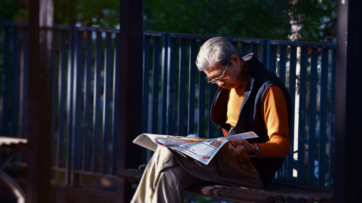Boomer language represented by an old man reading a newspaper while sitting outside