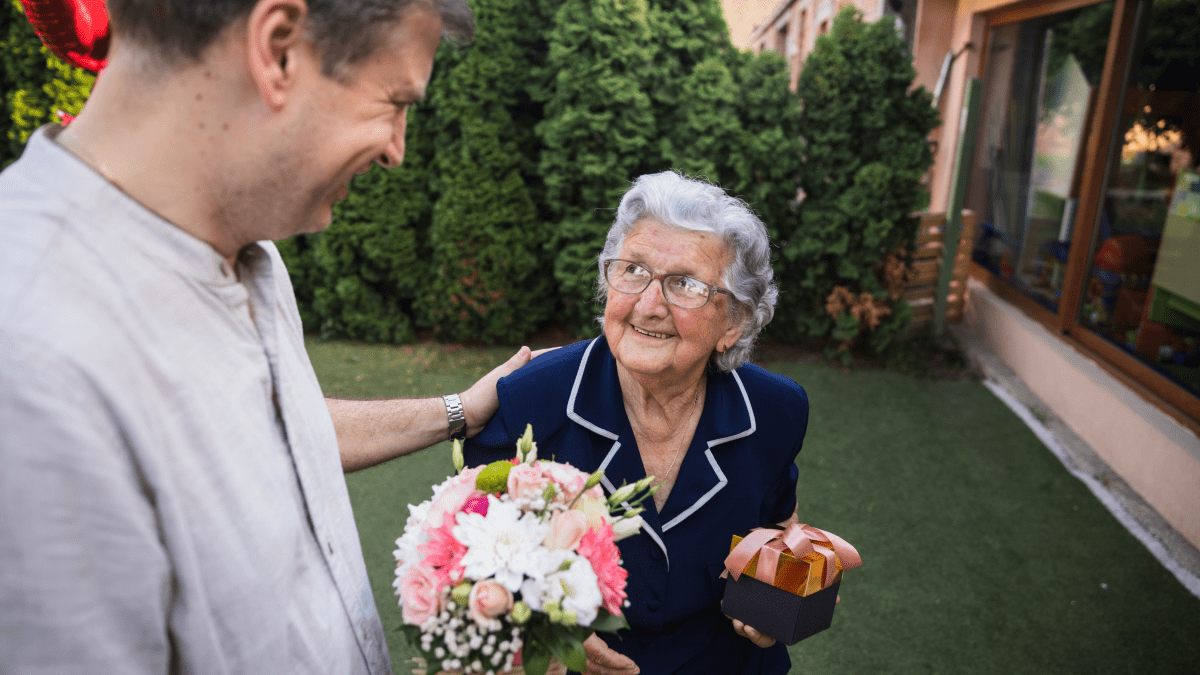man giving bouquet of flowers to smiling short old woman compliments in russian