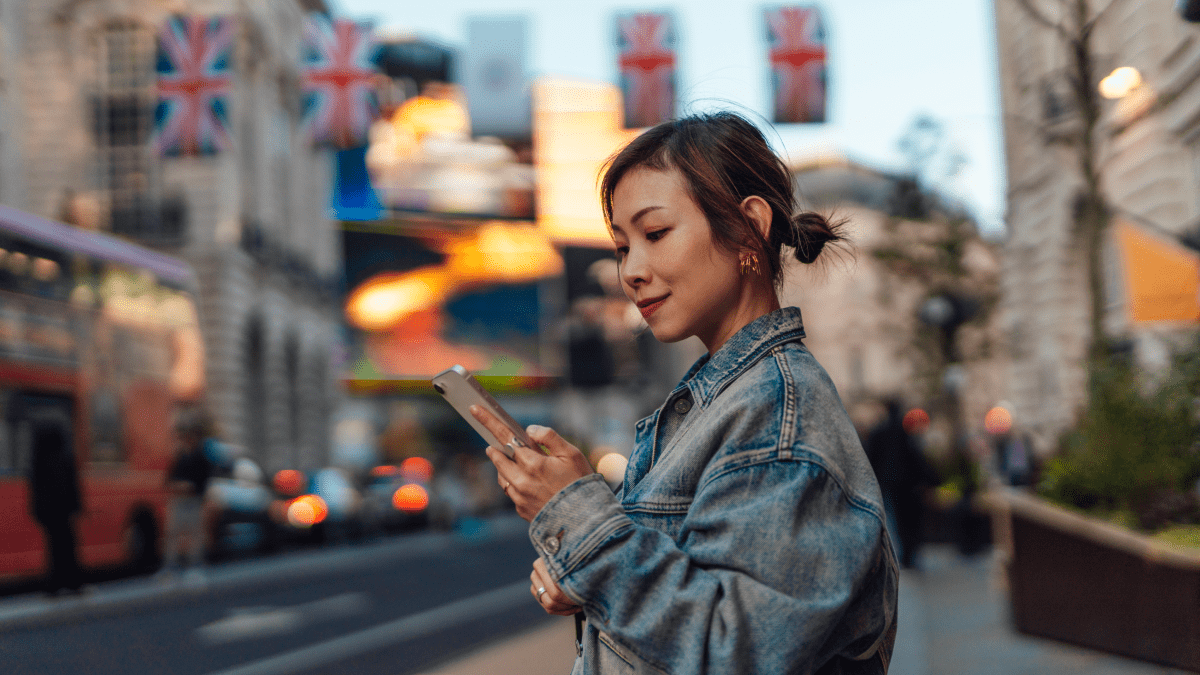 The most common English verbs represented by a young woman standing in the middle of a street in London looking at her phone.